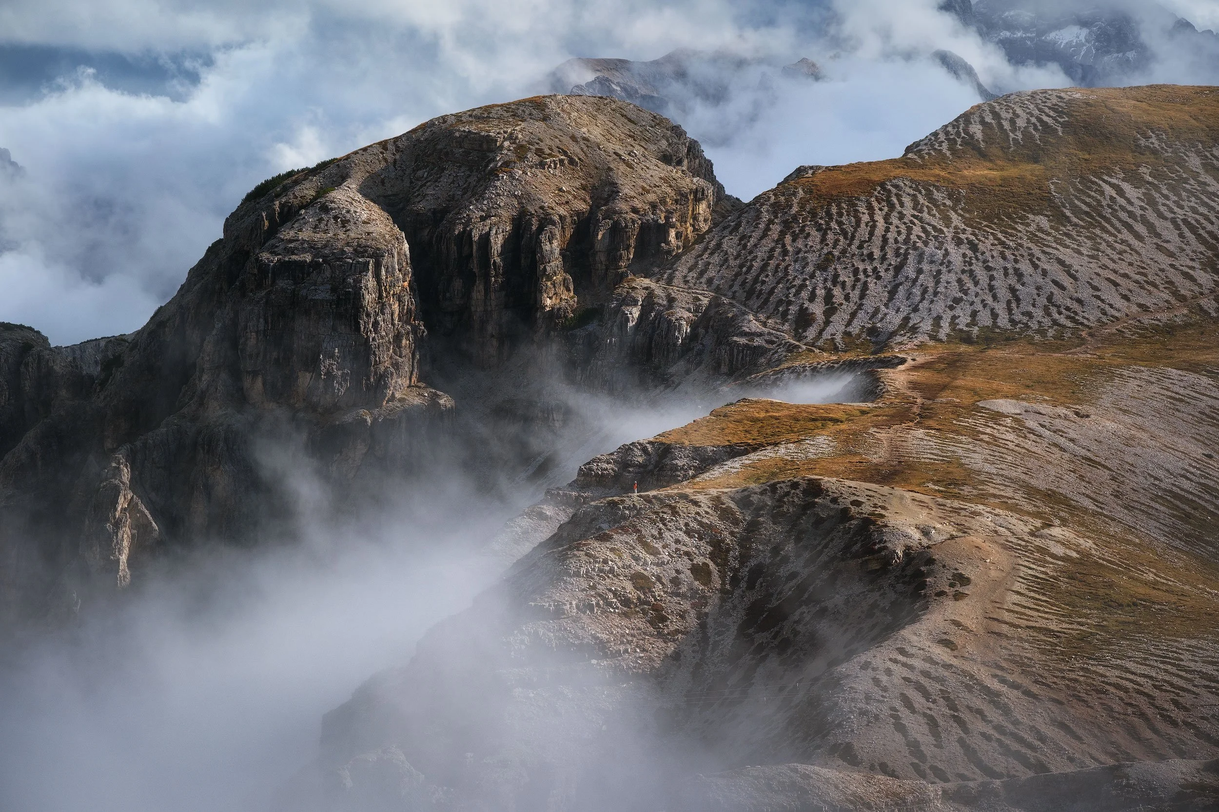 Cadini di Misurina in the Italian Dolomites with rugged peaks, mist or clouds in the valleys, and brownish terrain.