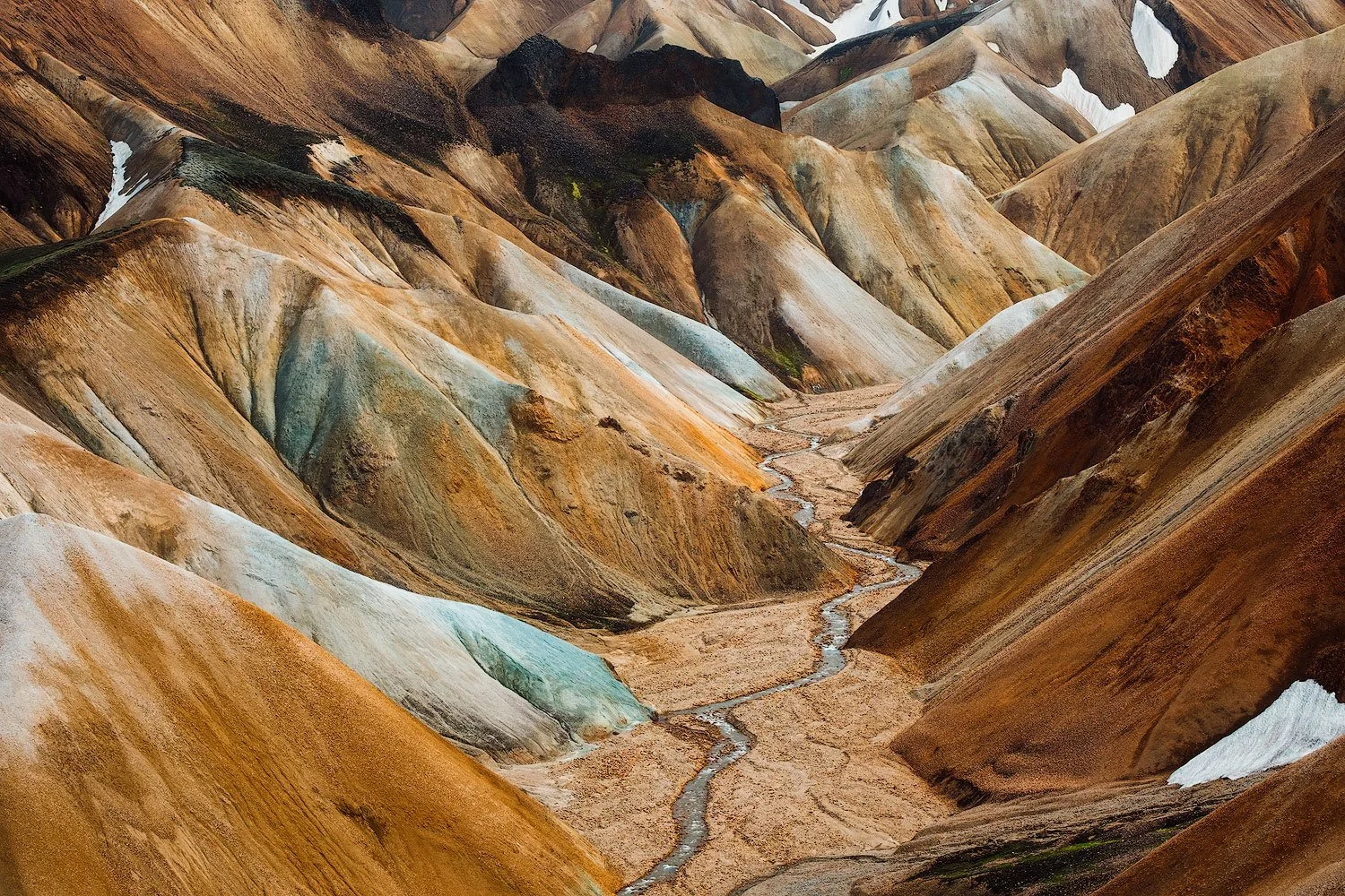 Colorful, layered mountains with a winding creek running through a valley in Landmannalaugar in the highlands of iceland.