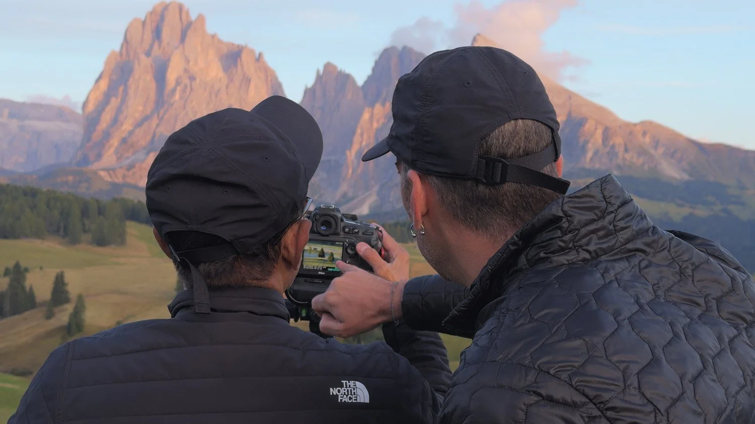 Two photographers checking a camera screen with the peaks of Alpe di Siusi in the background.