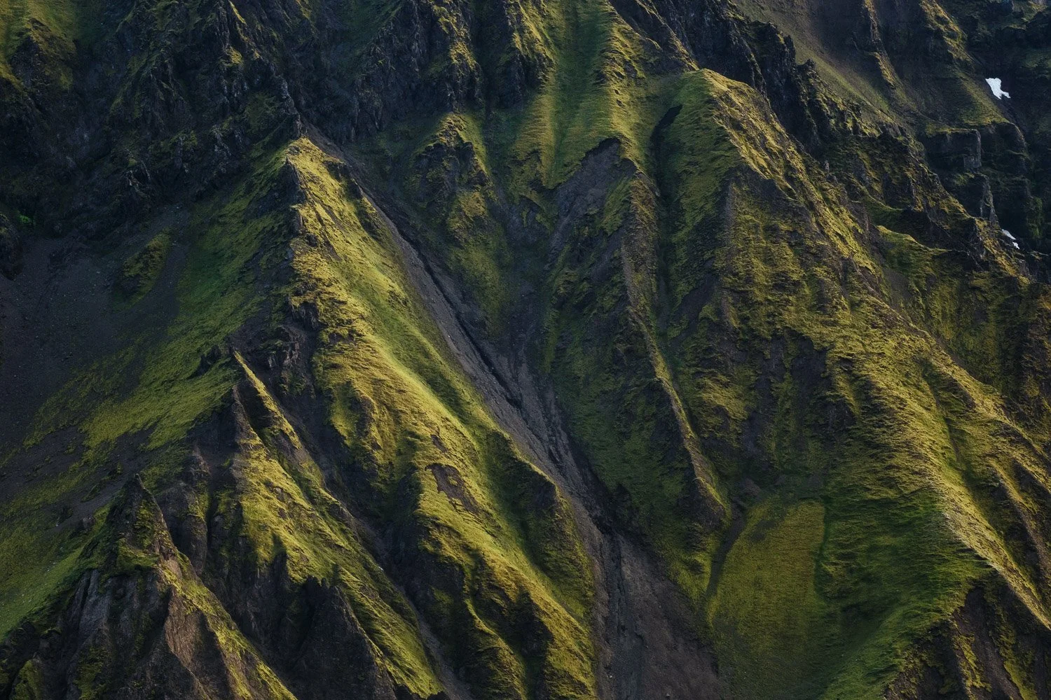 Sunlight and shadow across steep, moss-covered mountain ridges and gullies in Mælifellssandur, Iceland. Photographed with the Sigma 100-400mm F5-6.3 DG DN OS | Contemporary.