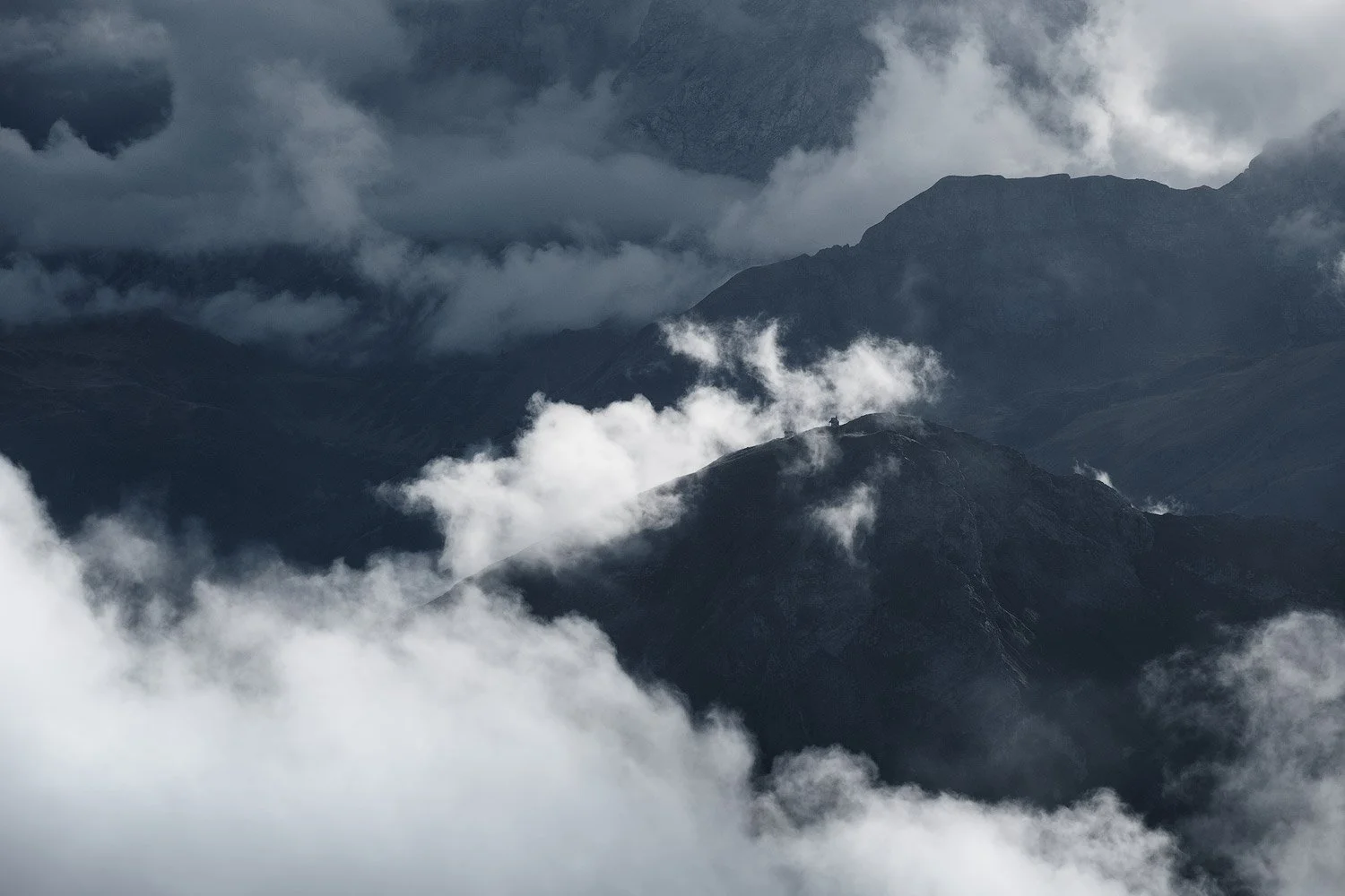 Layers of dark mountain ridges appearing through low clouds around Lagazuoi.