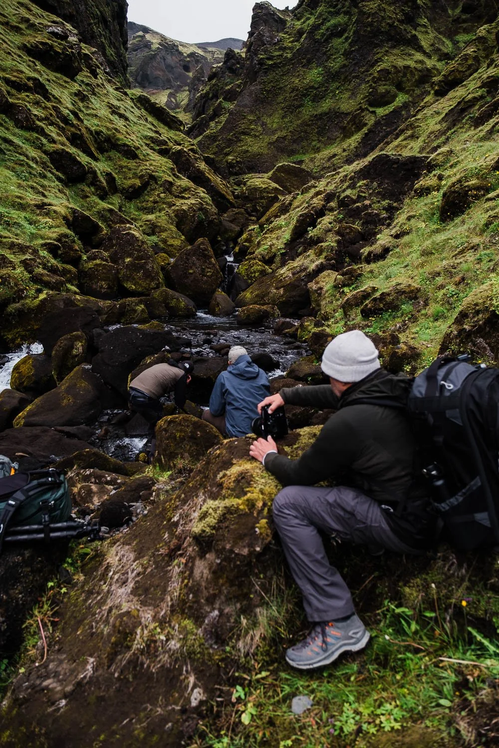 Three people exploring a rocky stream in a moss-covered canyon in Iceland.