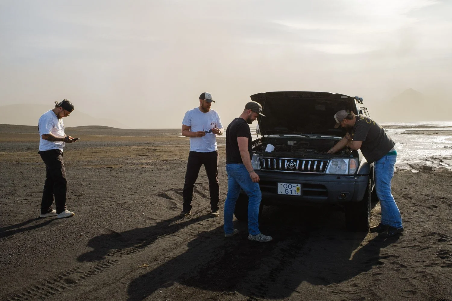 Four Icelandic fishermen gathered around an open 4x4 engine on the black-sand plains near Mælifell.