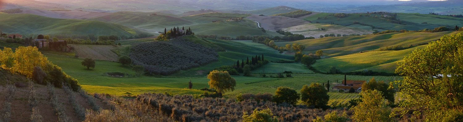 Golden sunrise light beginning to shape the rolling hills and farmland of Tuscany during early morning landscape photography.