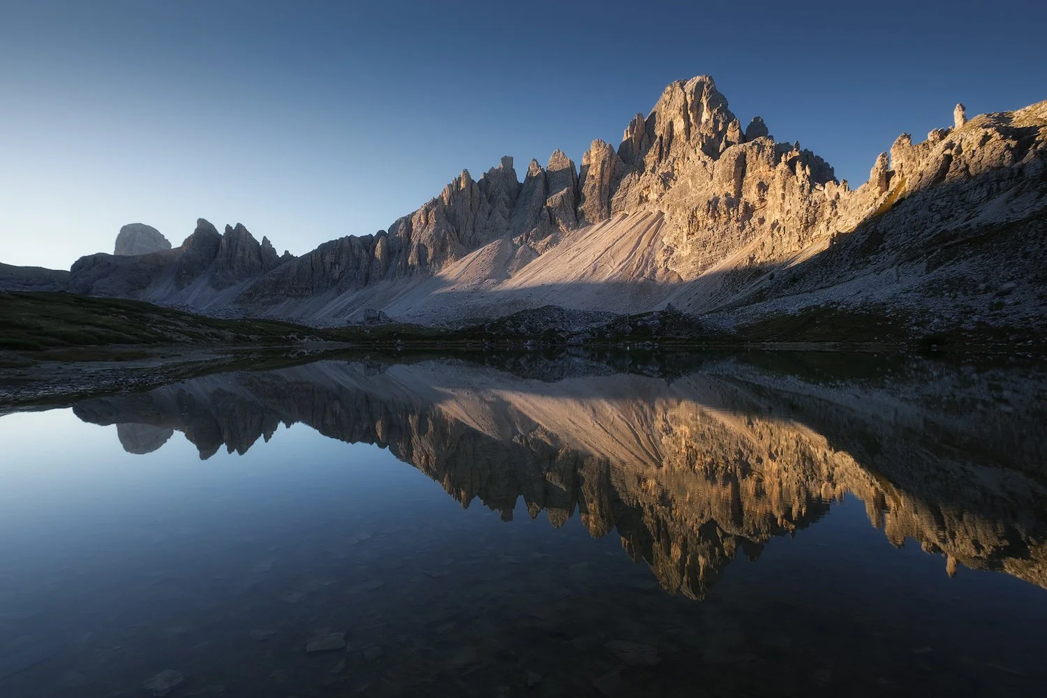Sunlit rocky peaks reflected in still water at Laghi dei Piani in the Dolomites.