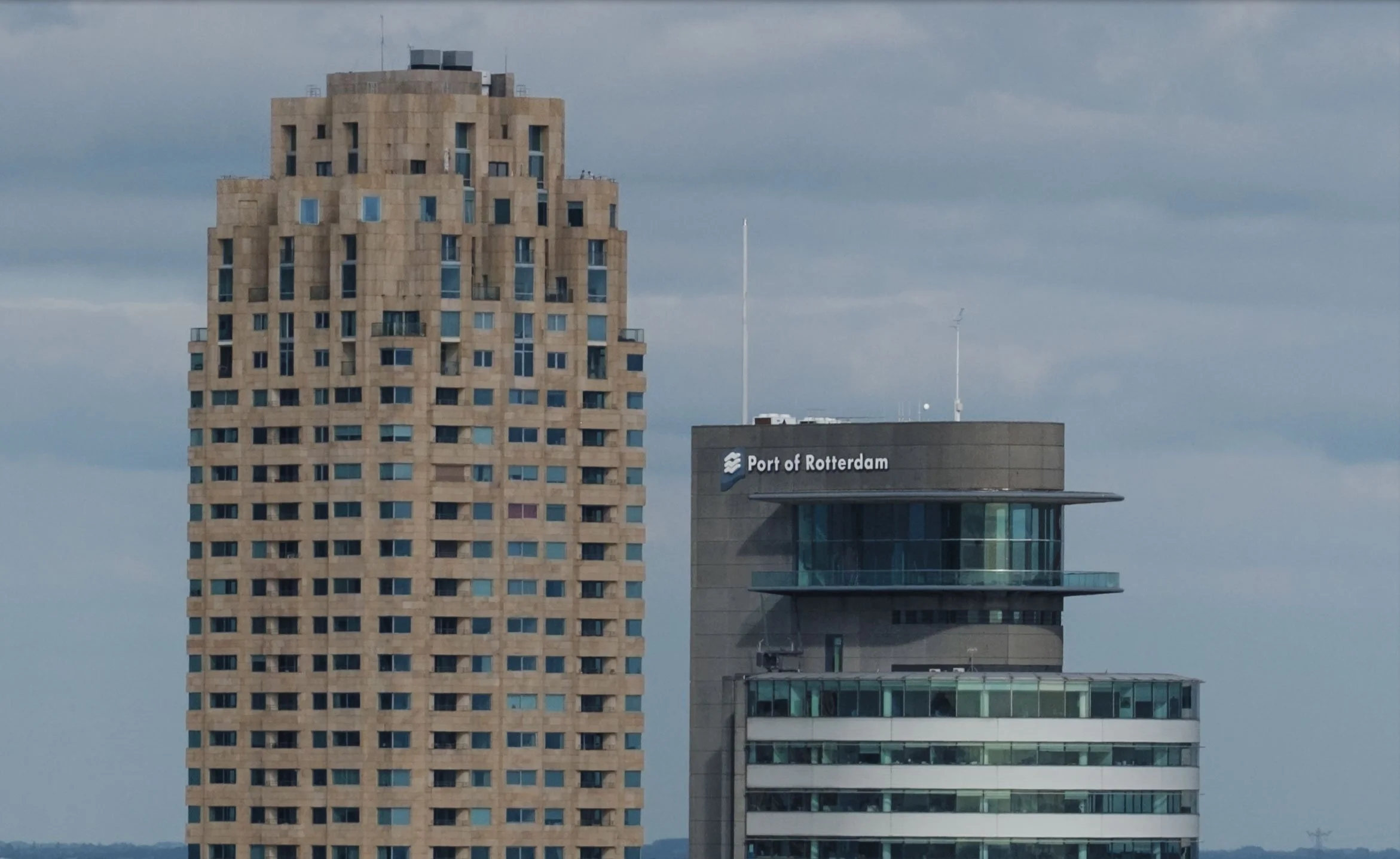 100% crop view of Rotterdam high-rises, including the Port of Rotterdam headquarters, beneath an overcast sky.