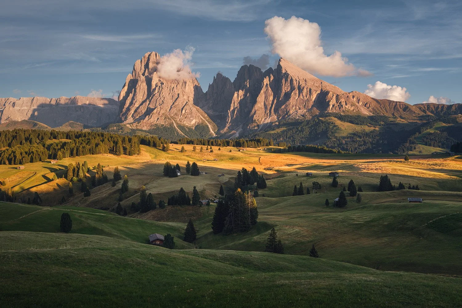 Evening sunlight across the rolling meadows of Alpe di Siusi, with Sassolungo and Sassopiatto beyond.