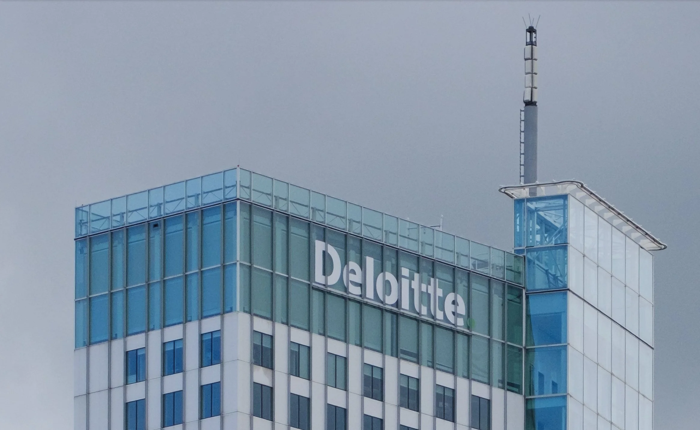 100% crop - Close-up of the Deloitte sign and glass rooftop structure on a Rotterdam high-rise.