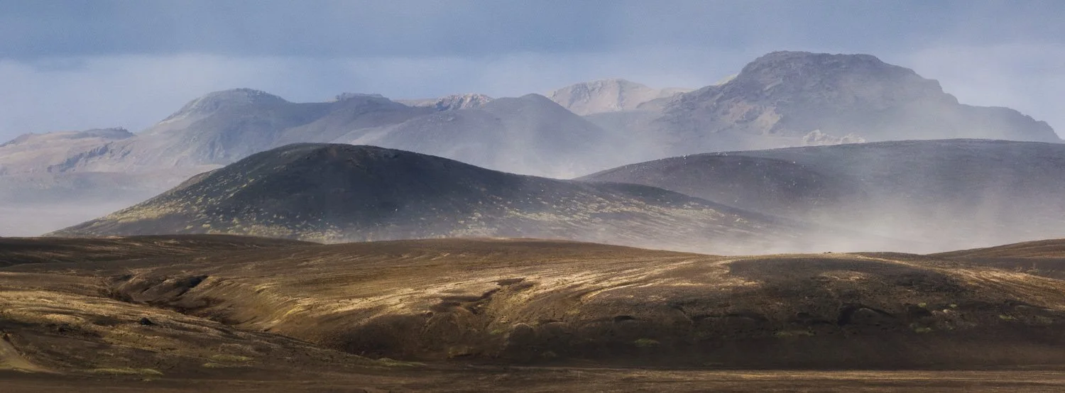 Layers of dark volcanic mountains partially obscured by windblown sand in the Icelandic Highlands.