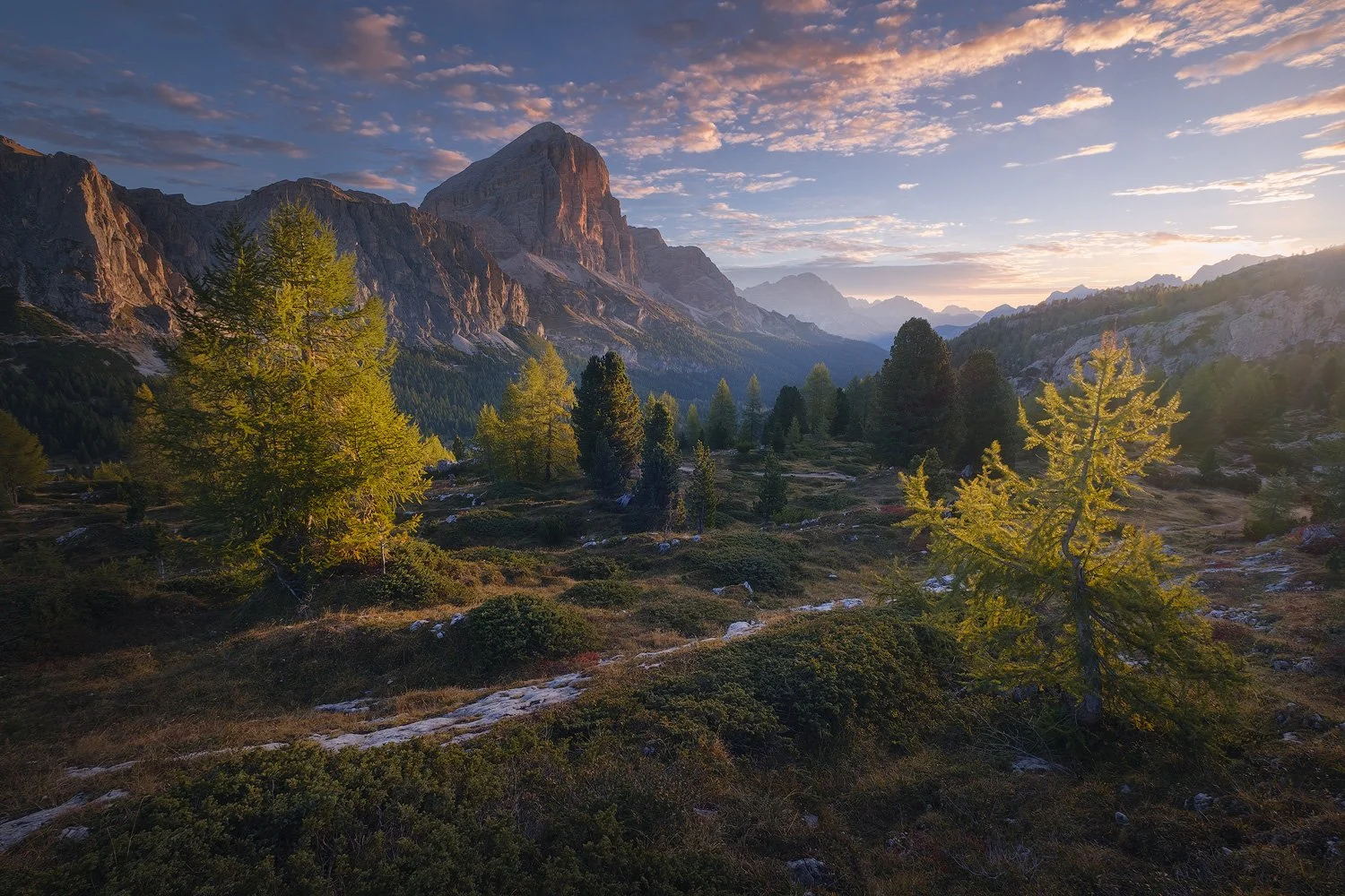 Sunrise light reaching rocky peaks and autumn larches near Passo Falzarego during the Dolomites photography workshop.