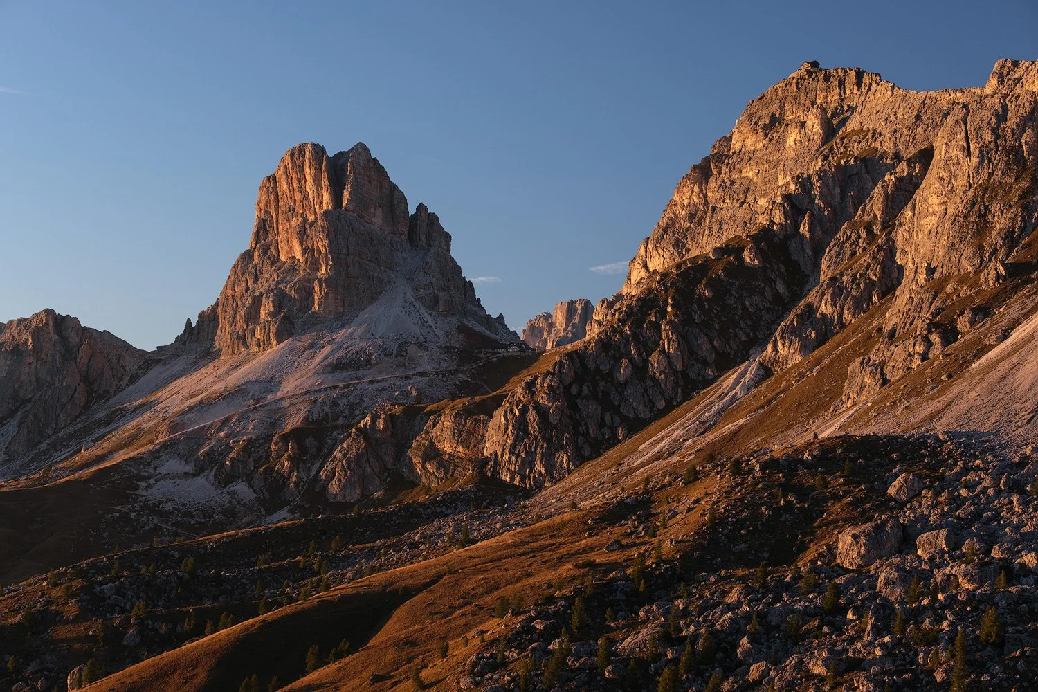 Warm evening light on the rocky peaks and autumn slopes of Passo Giau beneath a clear blue sky.