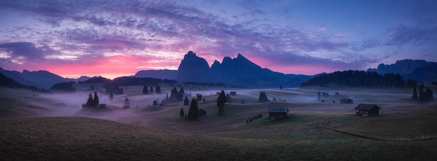 Xpan format pink and purple sunrise above Sassolungo and Sassopiatto, with mist spreading across the meadows of Alpe di Siusi.