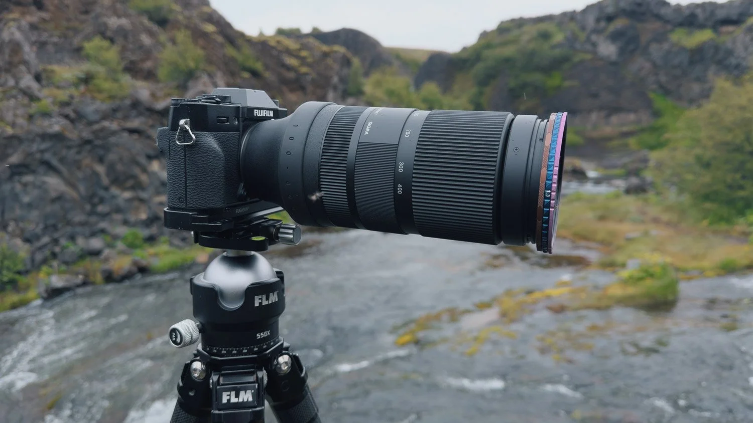 Fujifilm X camera and Sigma 100–400mm mounted by the camera body on an FLM tripod beside a stream in the Icelandic Highlands.