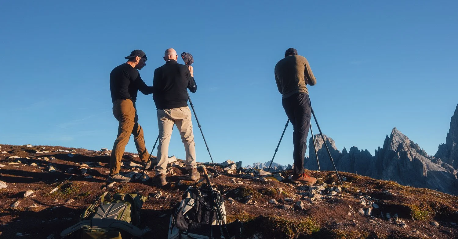 Workshop participants photographing Cadini di Misurina from a rocky ridge beneath clear blue skies.