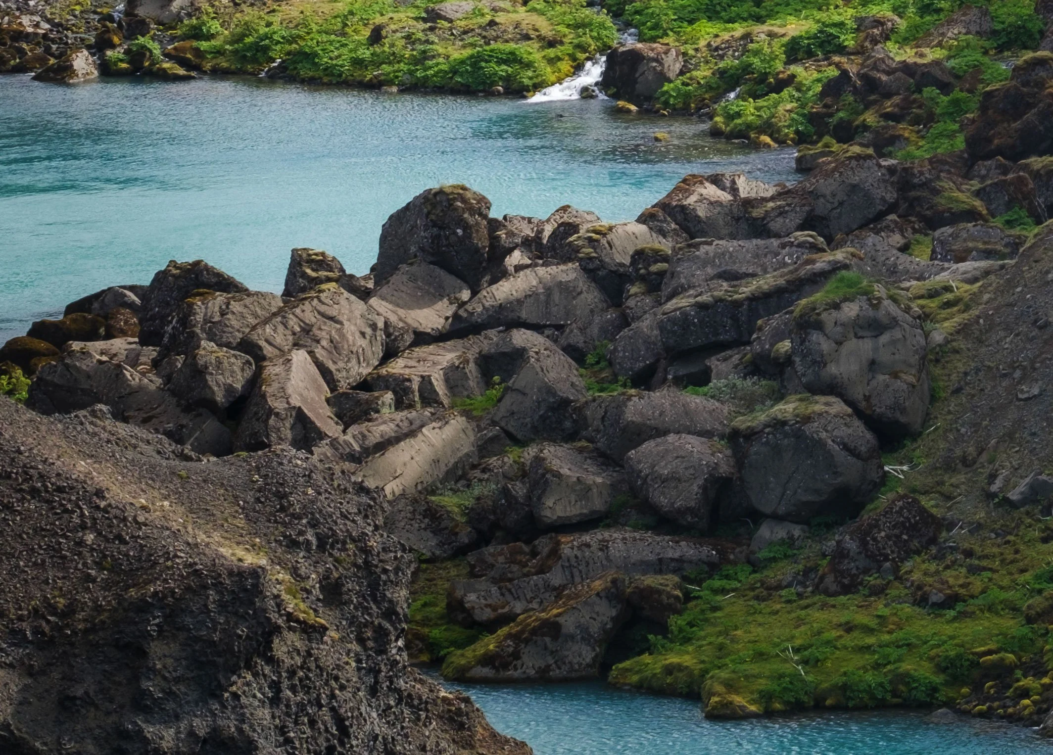 100% crop from the bottom-left of the Sigöldugljúfur photograph showing basalt boulders, moss and turquoise water.