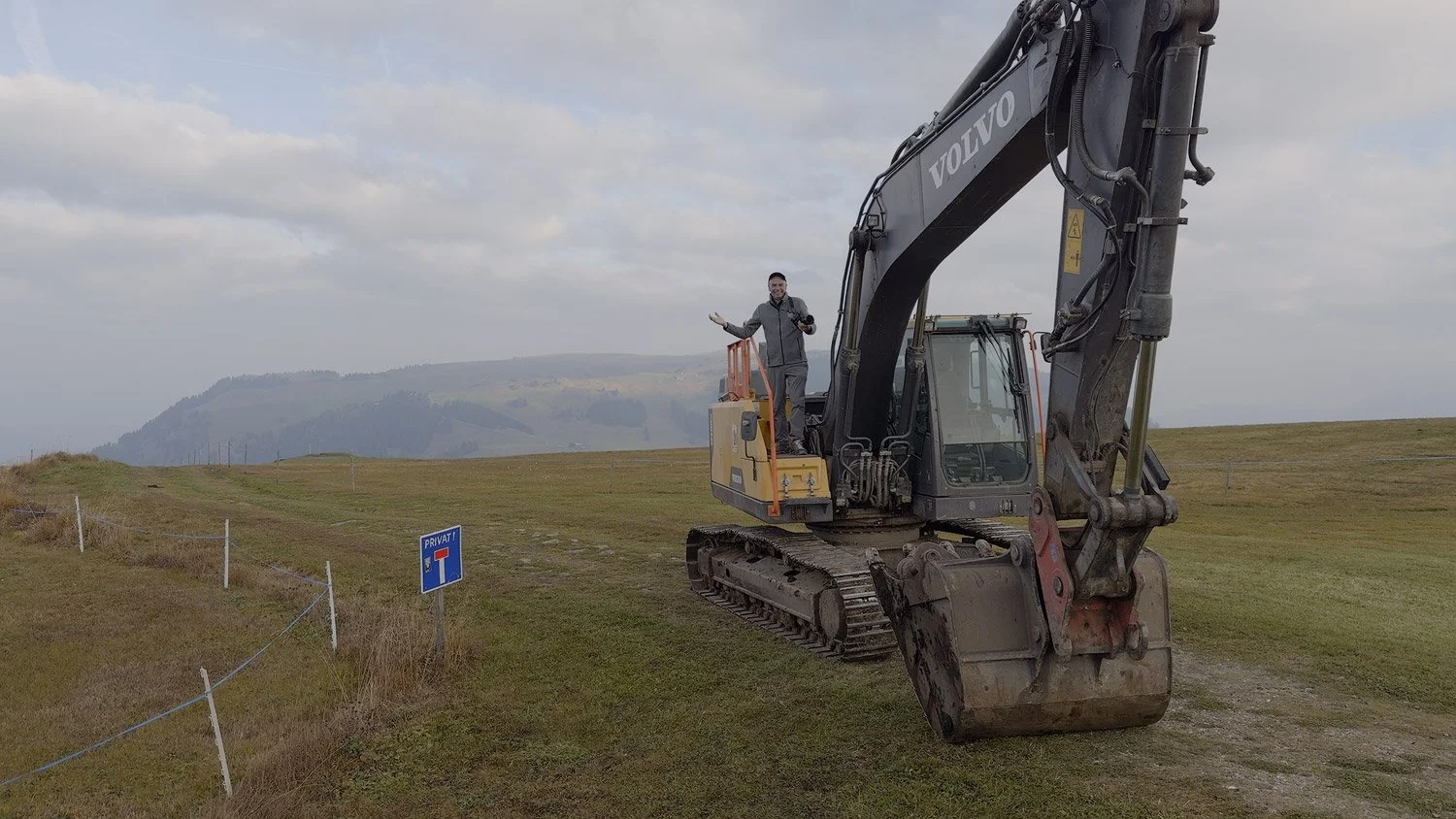 David seeking a higher photographic viewpoint beside a parked excavator on the meadows of Alpe di Siusi.