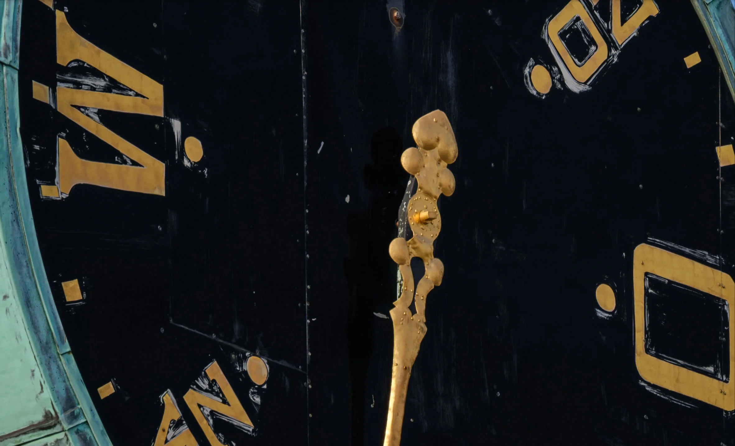 100% crop of the black-and-gold clock face showing weathering and fine surface detail.