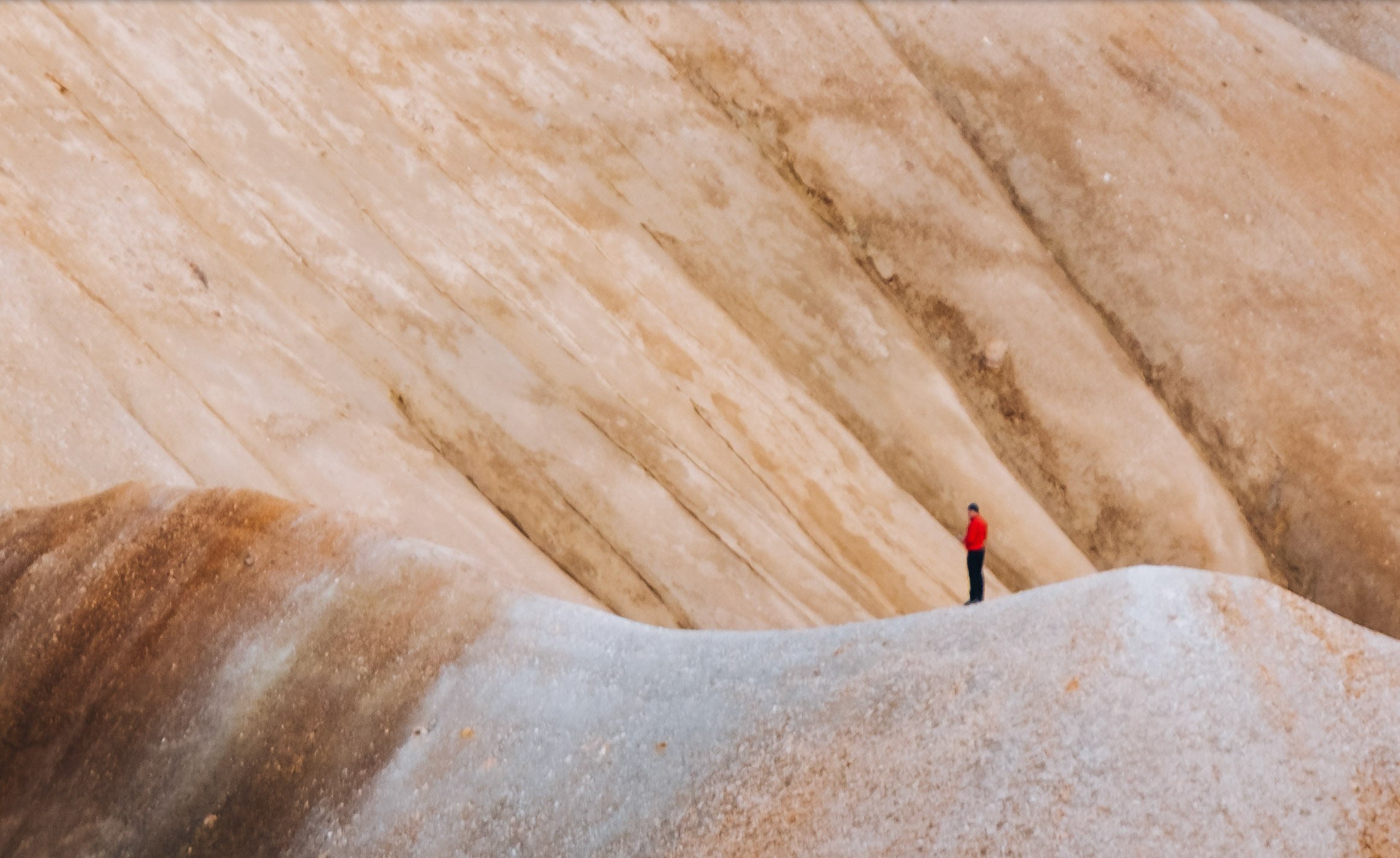 100% crop of a person in red against pale rhyolite slopes, showing softened detail in an Iceland photograph made with the Fujinon 50–140mm and 2× teleconverter.