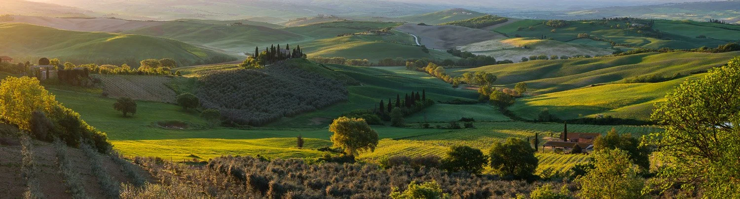 Golden hour panorama of Val d’Orcia in Tuscany with warm sunlight creating depth across rolling hills and farmland.