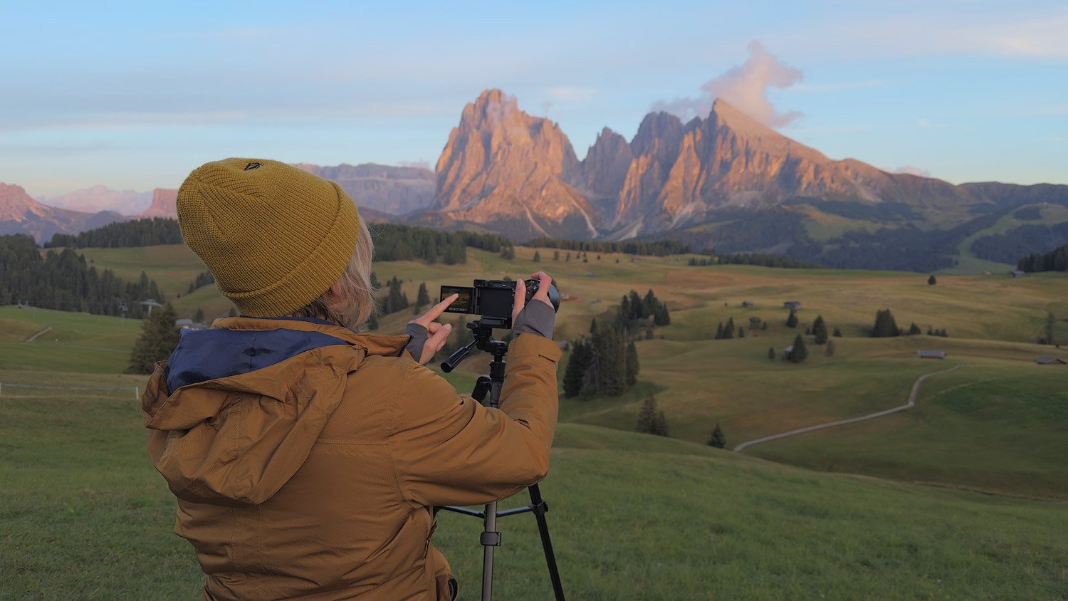 A workshop participant photographing Alpe di Siusi in evening light while wearing a yellow jacket and hat.