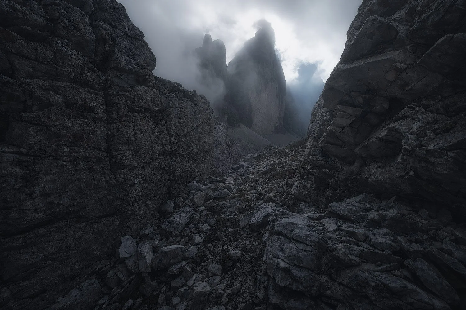 Dark rock walls framing the towers of Tre Cime di Lavaredo as they emerge through swirling cloud.