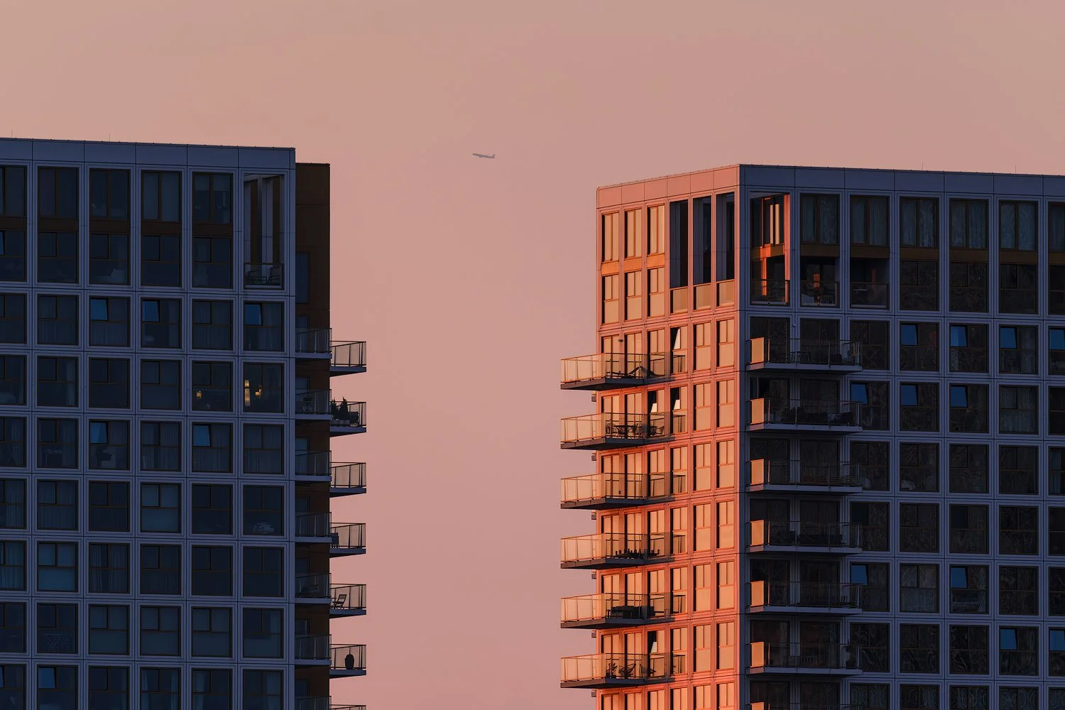 Two modern apartment towers illuminated by warm evening light with a small aircraft between them in Rotterdam.