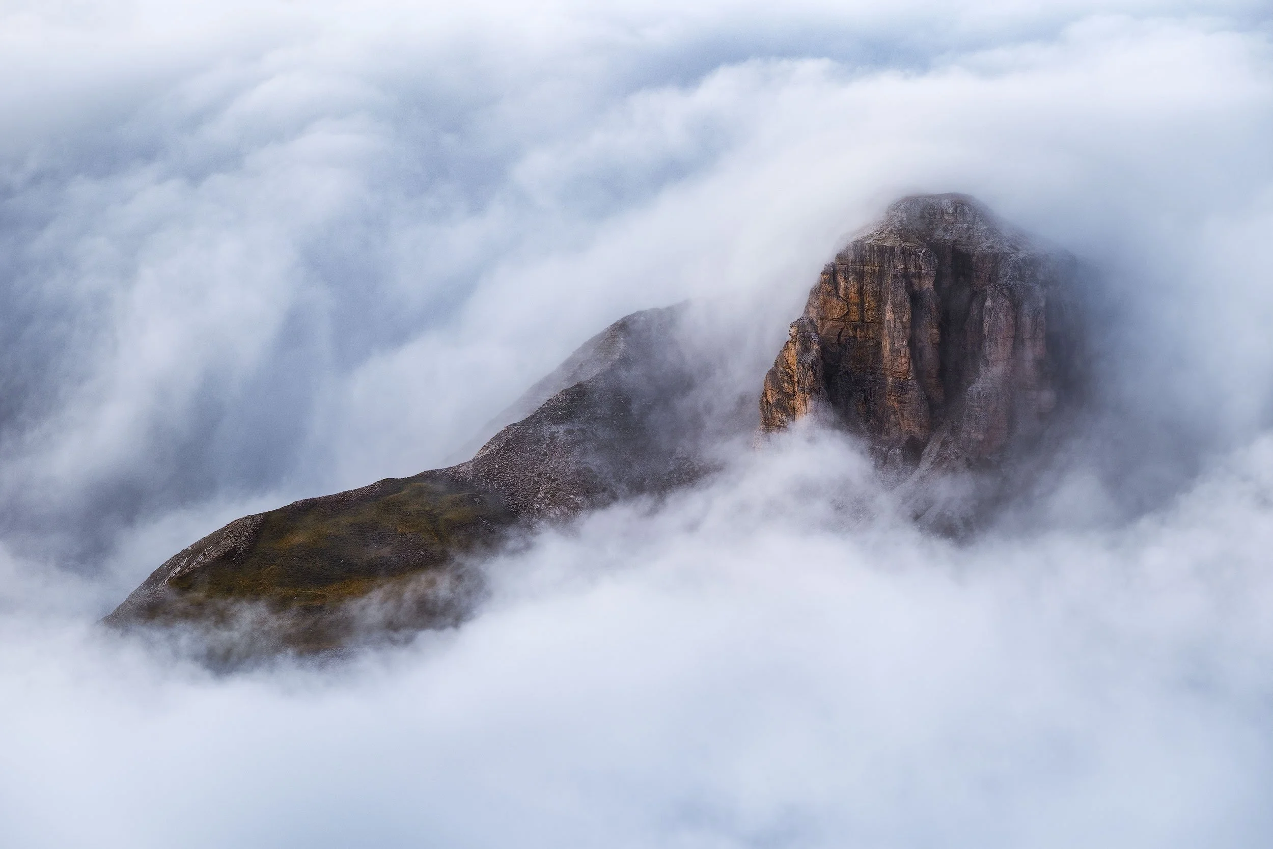 A mountain peak in the Dolomites partially obscured by clouds and fog.