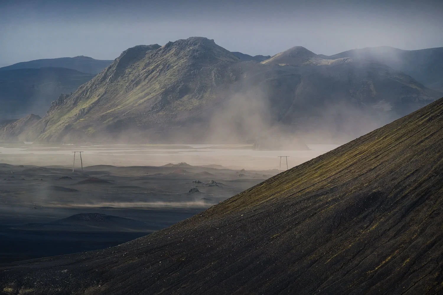 Windblown sand sweeping across a black volcanic plain around an off-road vehicle in the southern Icelandic Highlands.