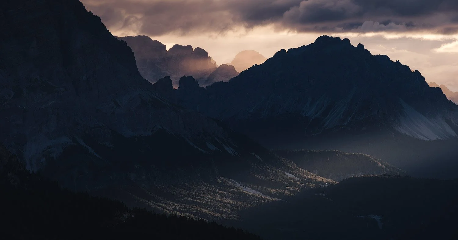 Light breaking through clouds over dark mountain ridges near Passo Falzarego.