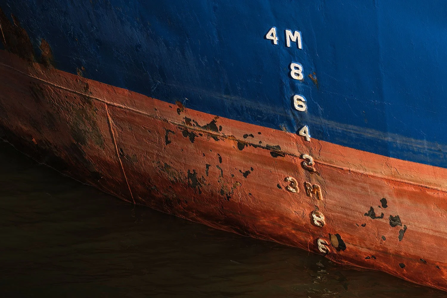 Weathered blue-and-red ship hull with white draught markings meeting the dark water.