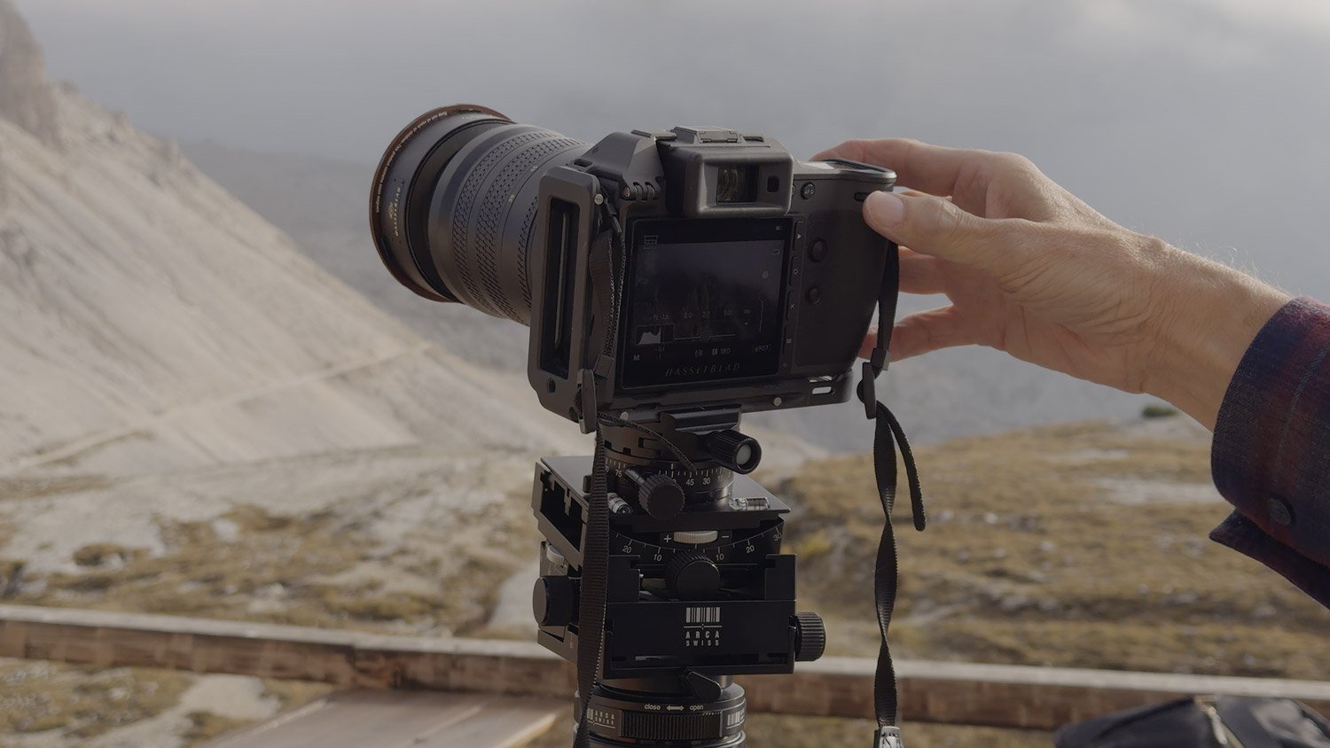 A participant adjusting a tripod-mounted Hasselblad camera with a long lens while photographing the mountains near Rifugio Locatelli.