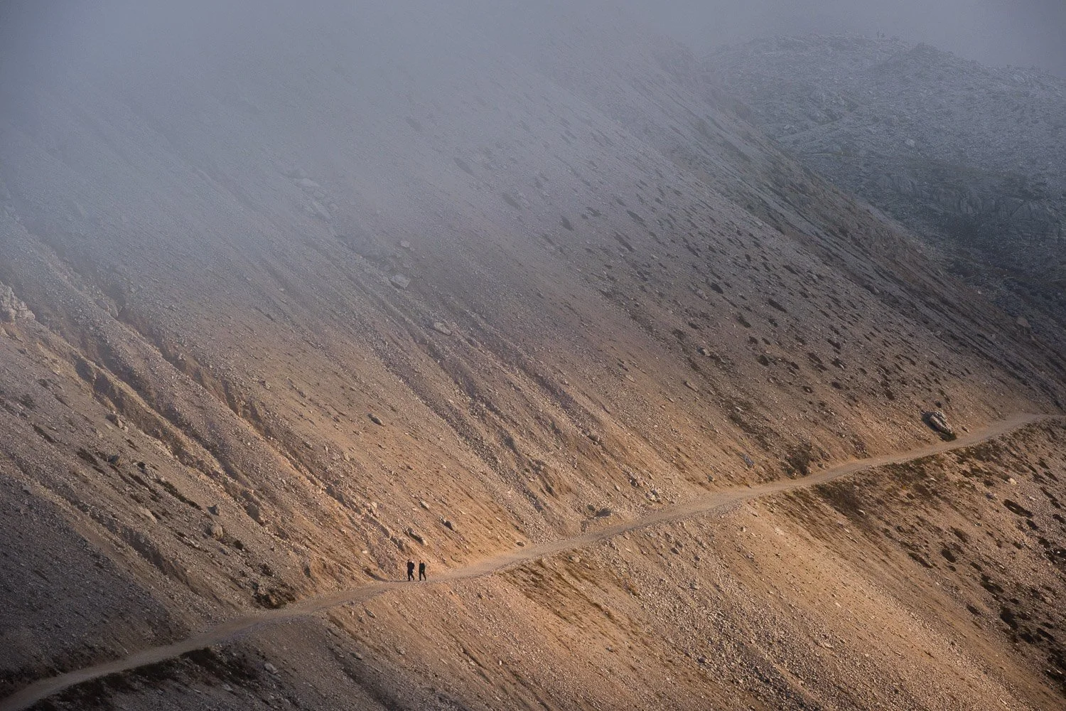 Small hikers crossing a sunlit scree slope beneath retreating cloud near Rifugio Locatelli in the Tre Cime area.