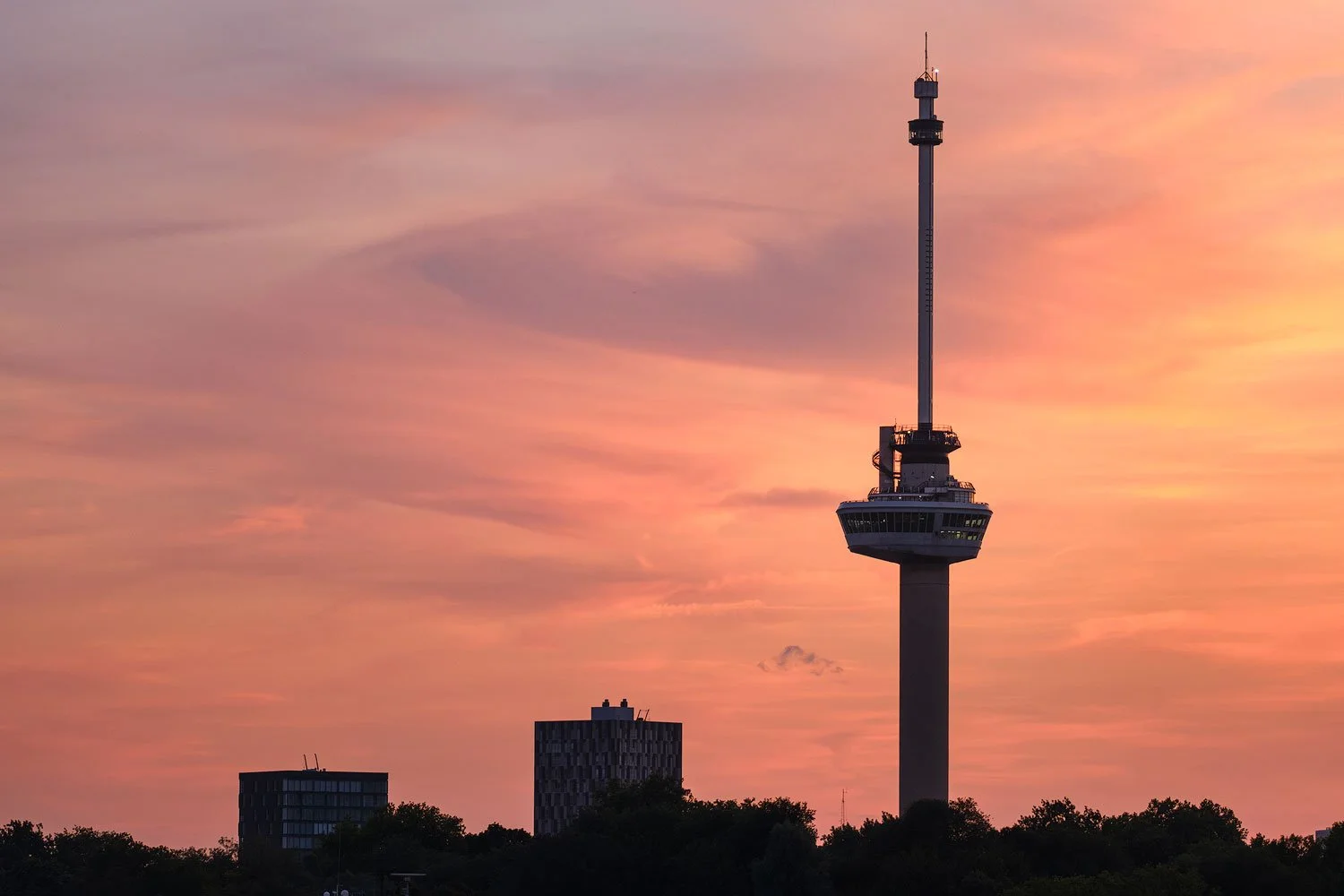 Wide view of the Euromast and Rotterdam skyline silhouetted against a dramatic orange sunset.