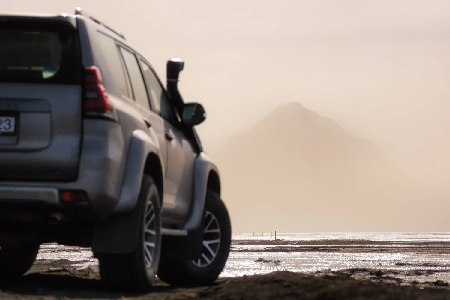 Silver 4x4 on black volcanic sand with Mælifell faintly visible through blowing sand in the distance. Photographed handheld with the Sigma 100-400mm F5-6.3 DG DN OS | Contemporary on the Fujifilm X-T4.