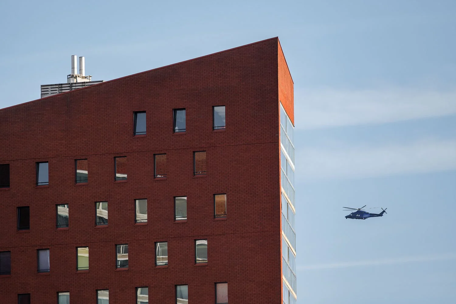 Red skyscraper high-rise and a helicopter crossing the blue sky above Rotterdam.