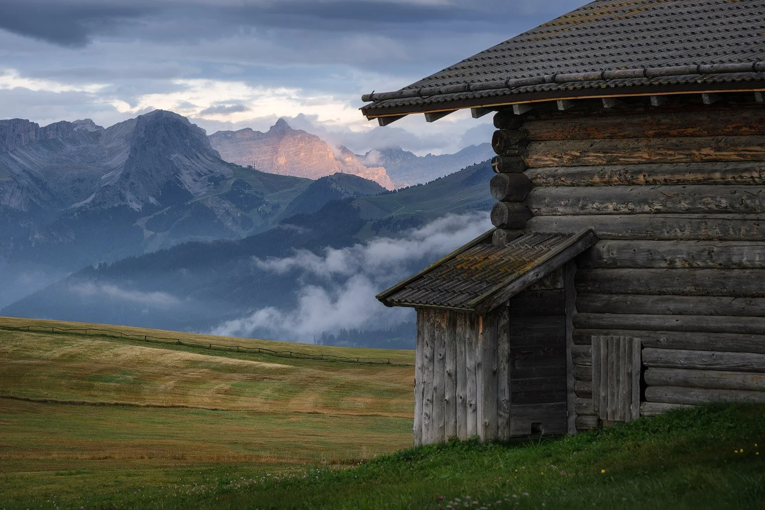 Weathered wooden walls of an alpine hut overlooking misty meadows and mountains at Alpe di Siusi.