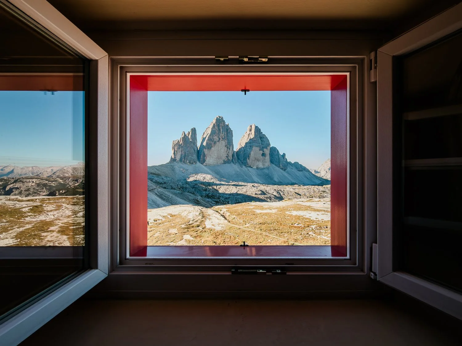 Tre Cime di Lavaredo framed by an open window inside the mountain hut.