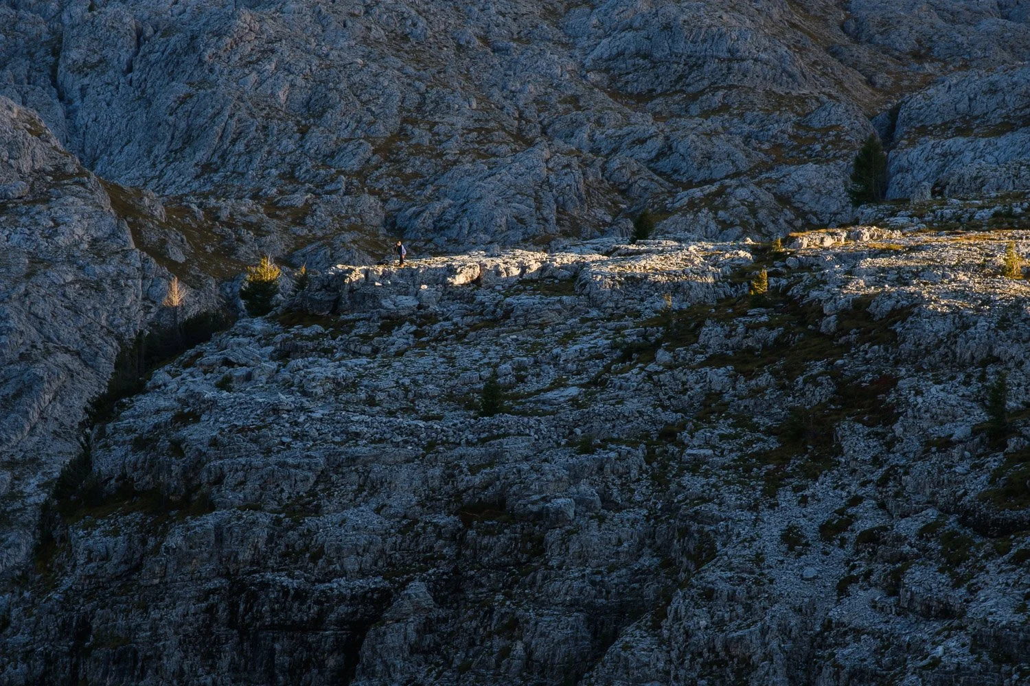 A narrow band of sunlight crossing rocky ground beneath shaded cliffs at Cinque Torri.