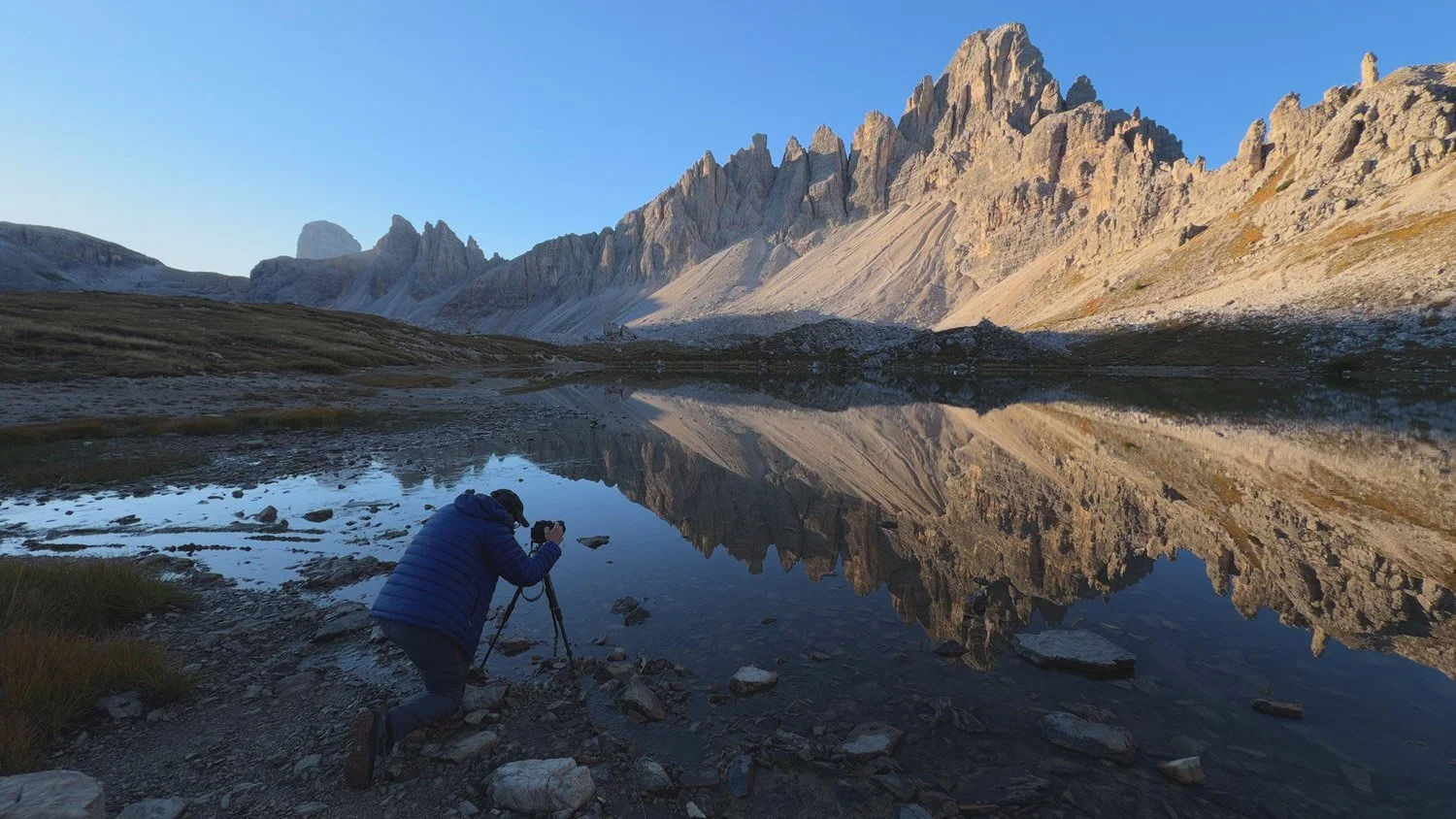 A workshop participant crouching beside an alpine lake to photograph mountain reflections at sunrise.