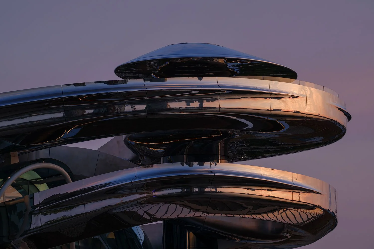 Curved mirrored sections of Fenix museum surroundings at sunset.