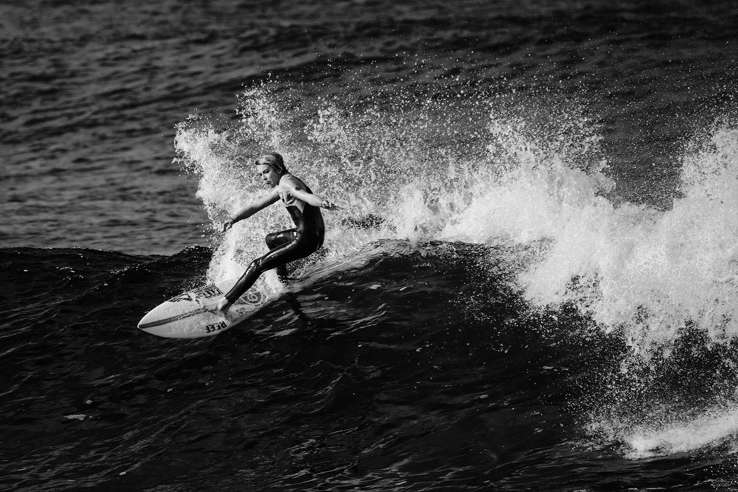 Black-and-white close-up of a surfer carving across a dark wave surrounded by spray in La Santa, Lanzarote.