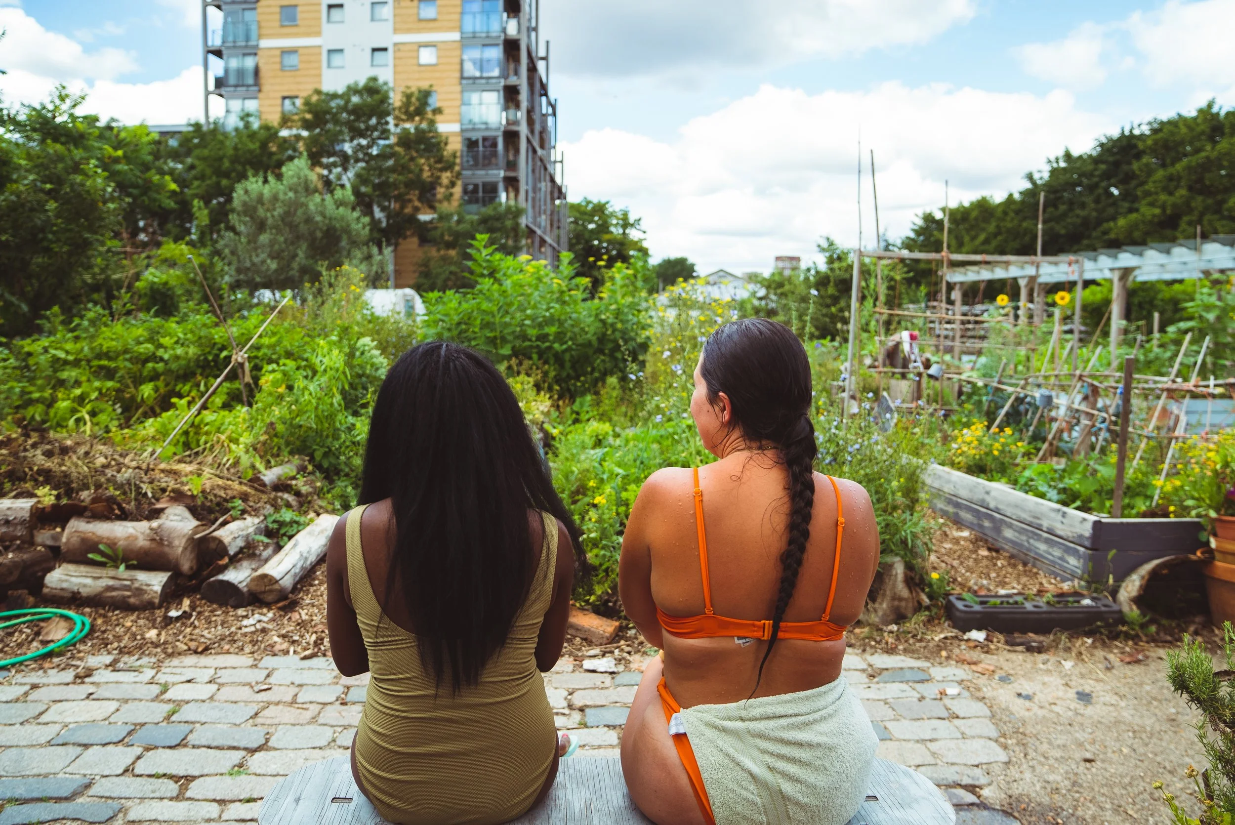 two sauna bathers with their back to the camera chatting in the garden peckham community sauna baths london