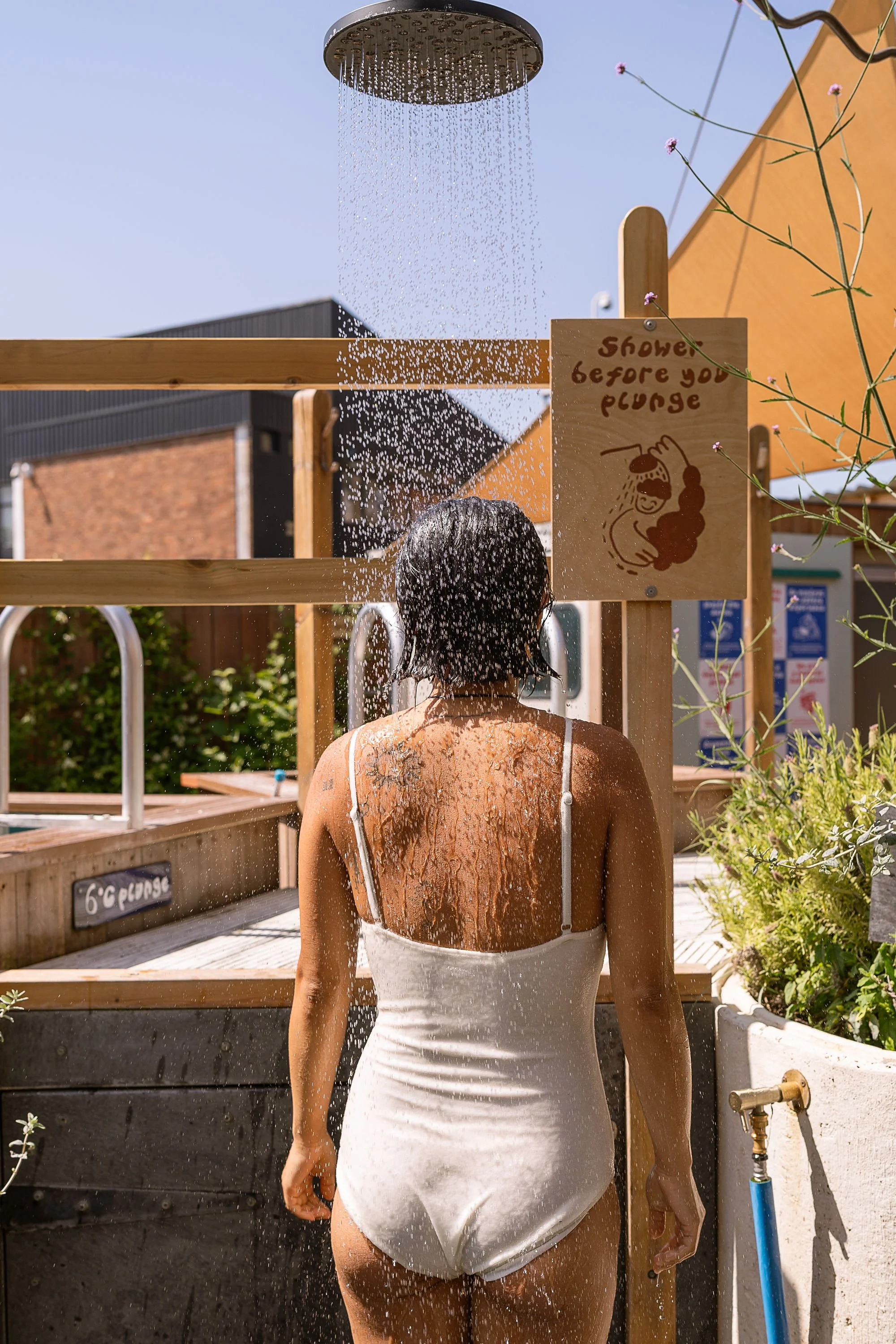 shower before you plunge wooden sign with bather in white swimsuit under the shower walthamstow community sauna