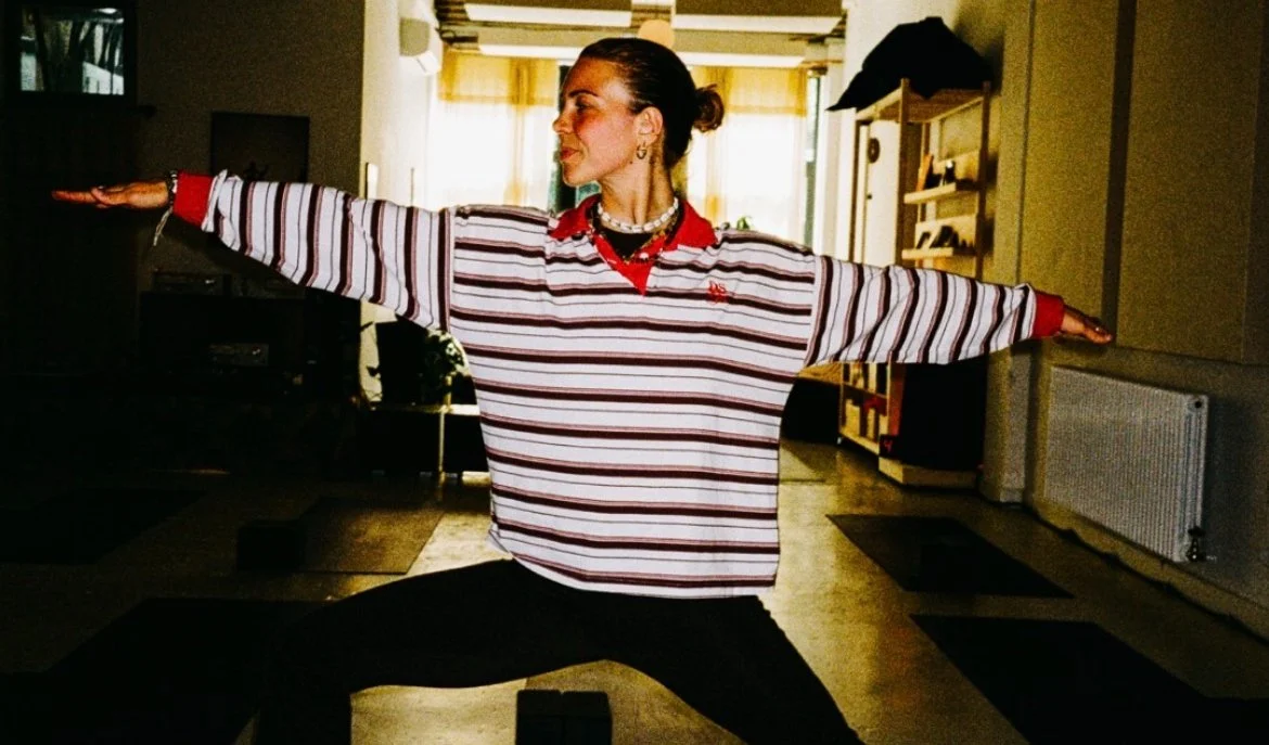 Woman in striped shirt practicing yoga in a well-lit room.