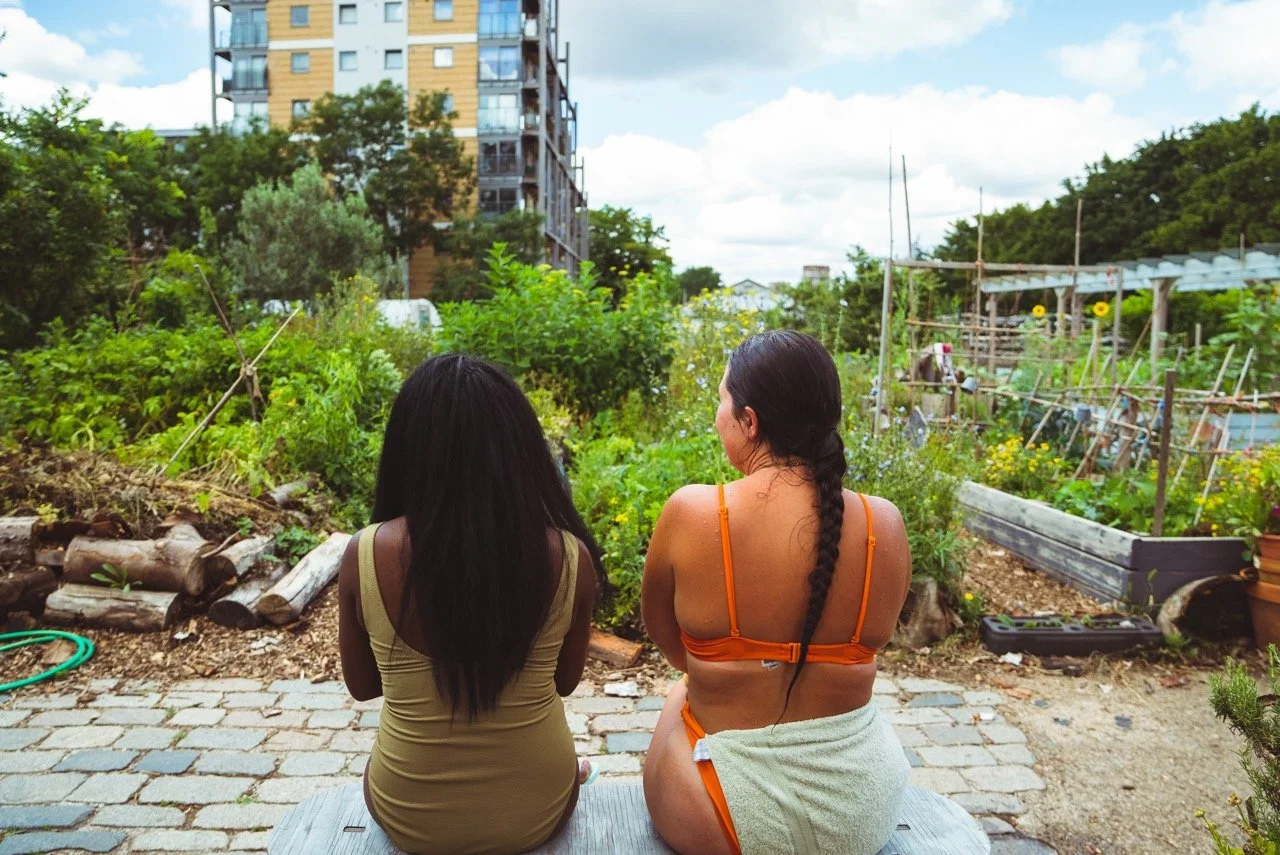 two sauna bathers in swimsuits with their back to the camera chatting in the garden peckham community sauna baths london