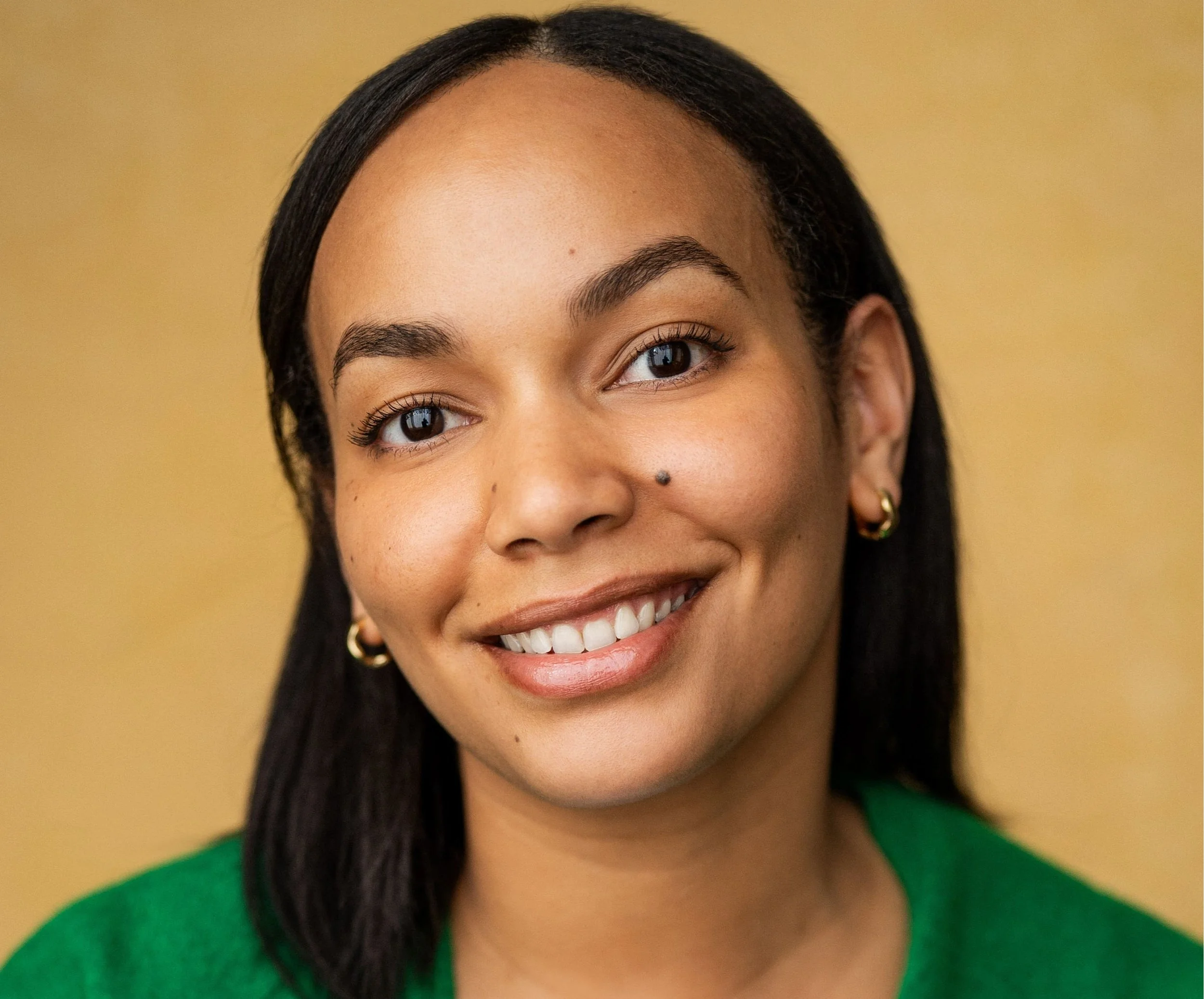 lady with green shirt, gold earrings smiling into camera with golden background
