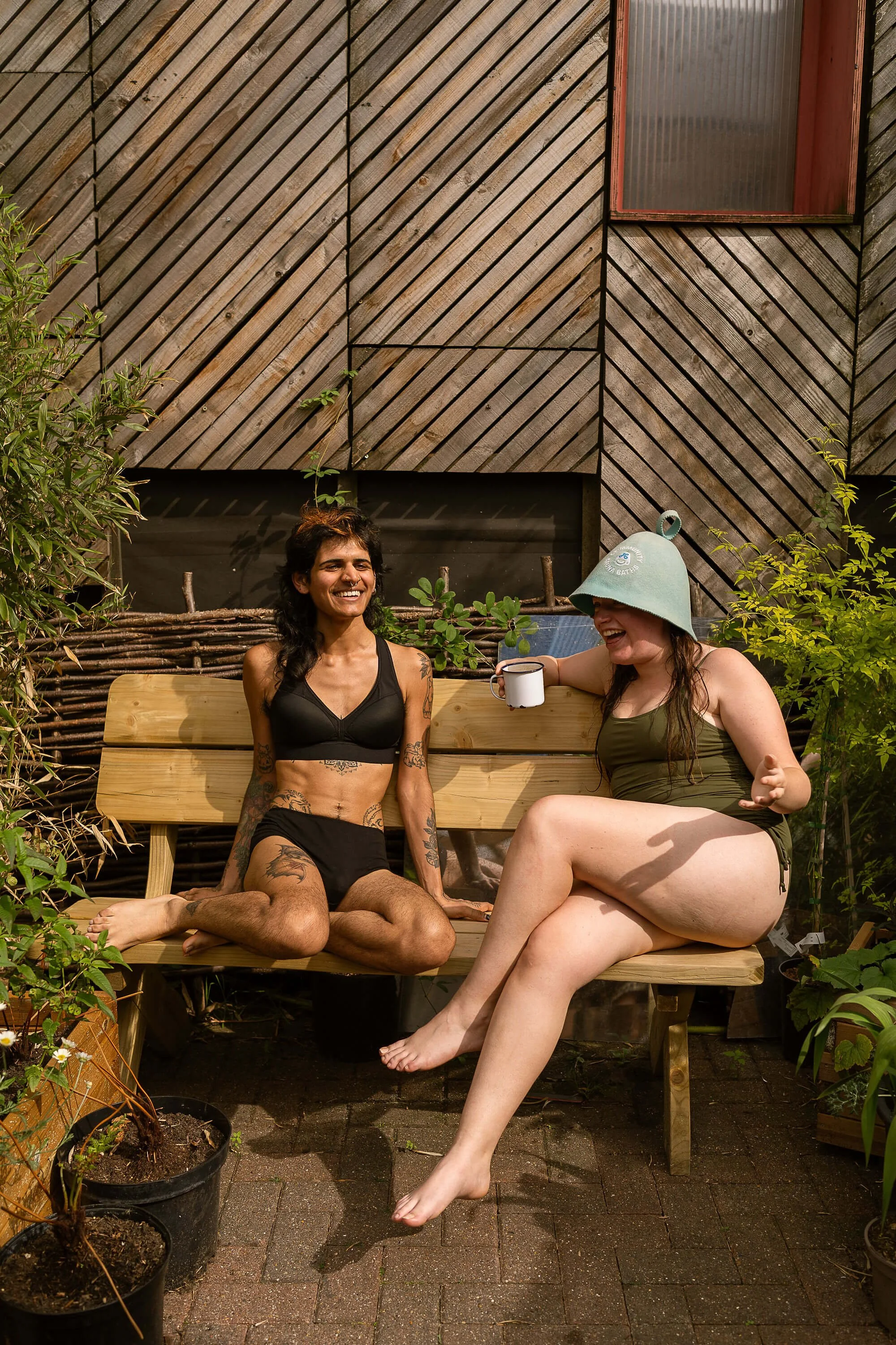 sauna goers sitting on a bench and enjoying the lovely weather smiling at Community Sauna Baths Hackney Wick London