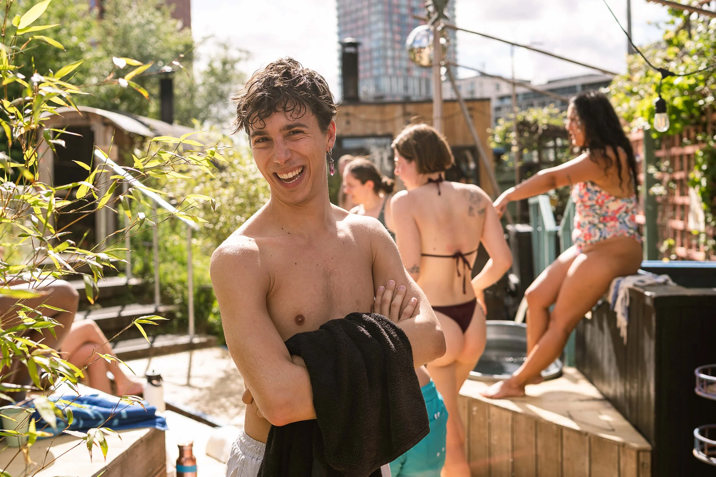 bather in swim shorts, holding towel smiling at camera in sunshine stratford community sauna baths