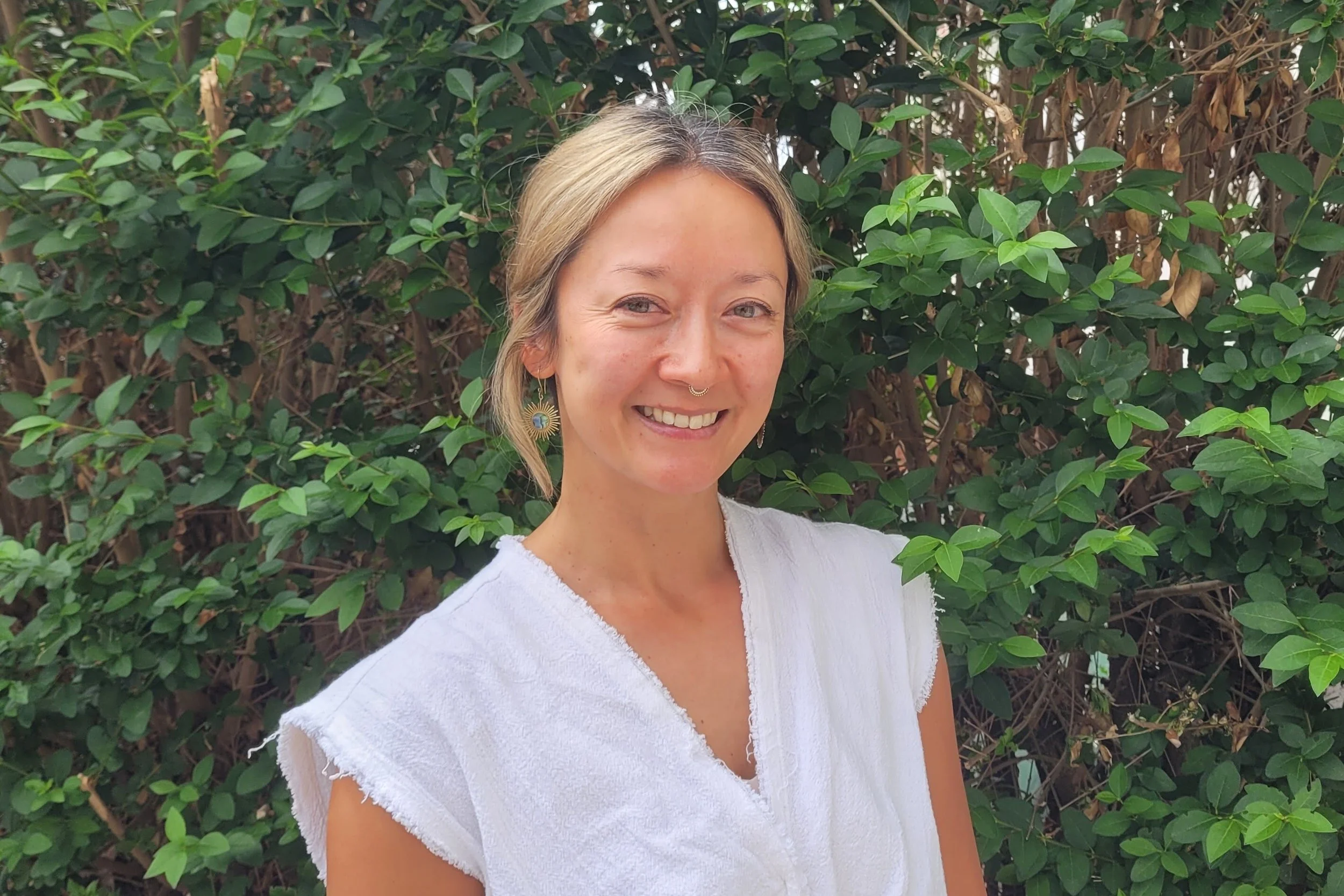 lady in white shirt smiling at camera in front of trees