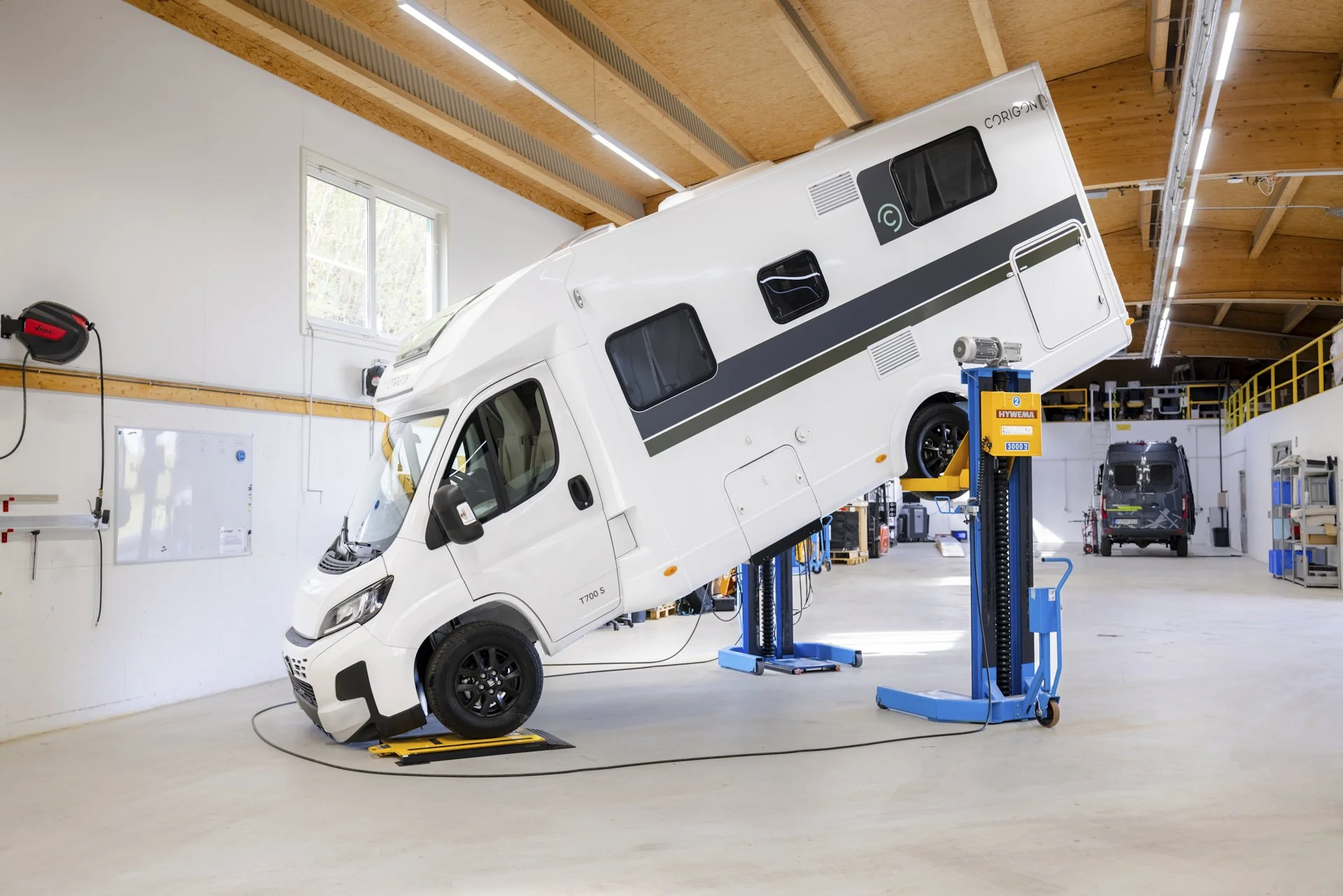 Ein weißer Wohnmobil im Prüfstand in einer Werkstatt, mit einer aufrecht stehenden Front und einem gezogenen Aufstelldach.